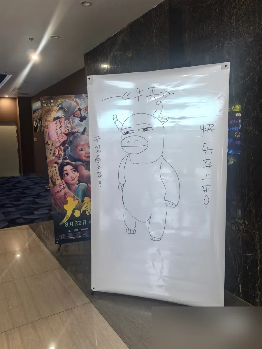 A hand-drawn Niu Lai poster in a Wuhan cinema reading 牛马看牛来 快乐马上来, with the account watermark blurred — 牛马 (niu ma)